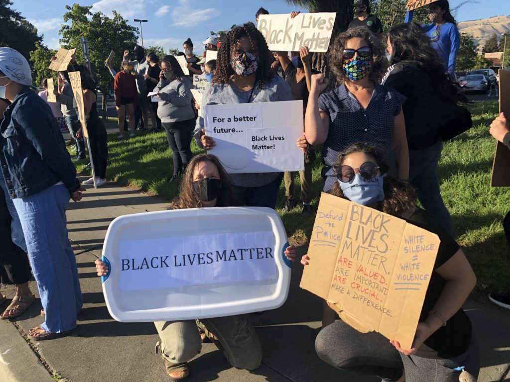 4 women are holding signs that read Black Lives Matter at a rally
