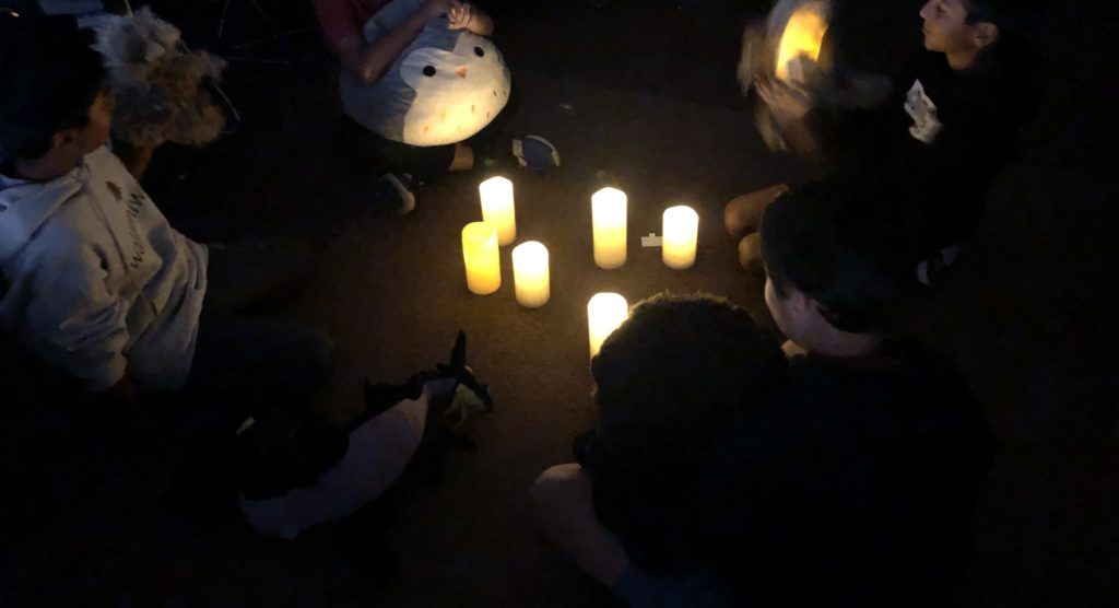 in the dark, a group of 6th grade students sit in a circle around 6 battery operated candles