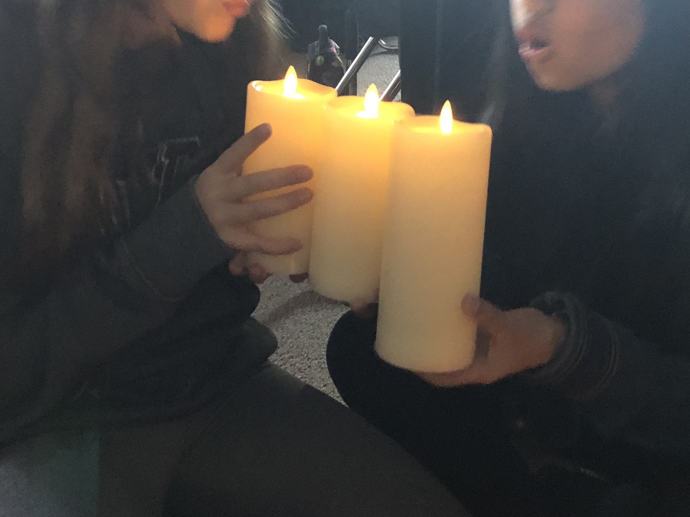 two girls hold battery operated pillar candles and attempt to blow them out