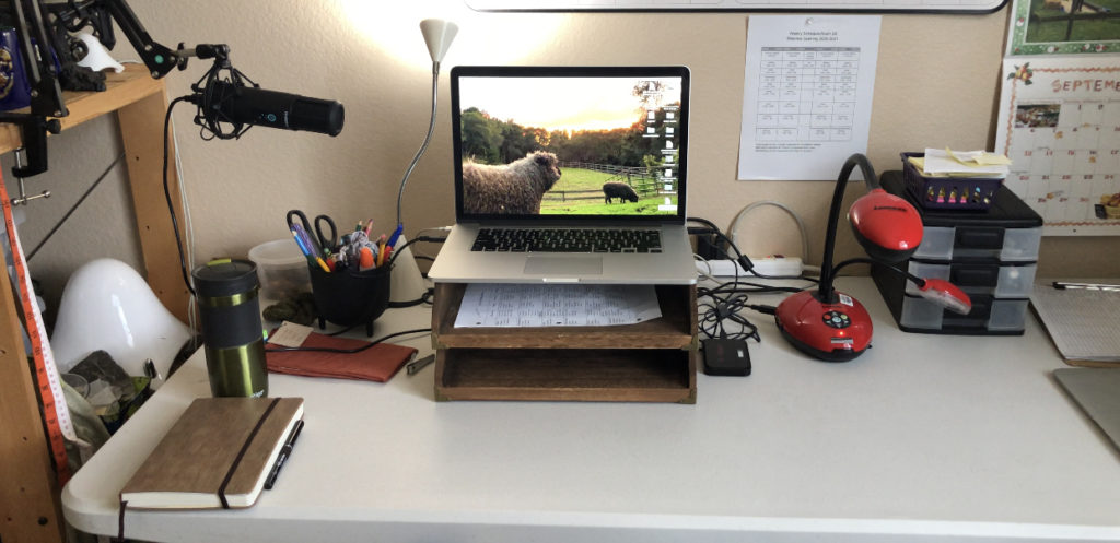 a macbook laptop with a sheep pictured on the desktop is centered on a desk with a microphone to the left and a document camera to the right